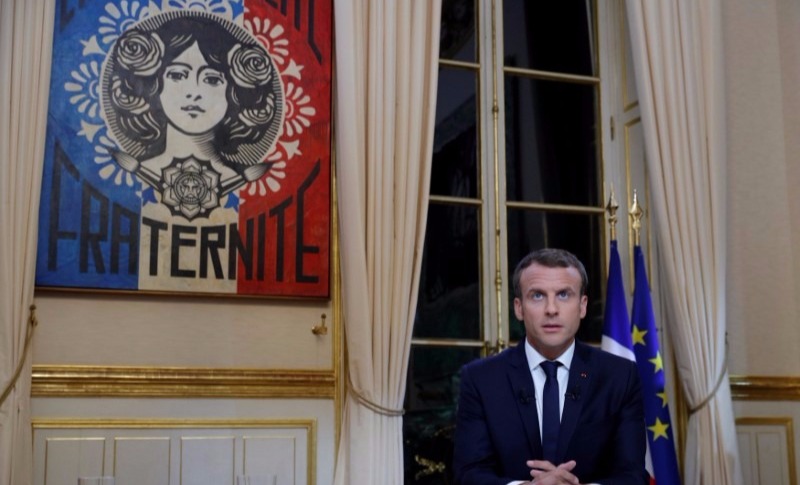 French President Emmanuel Macron sits in front of a Shepard Fairey poster before his first long live television interview on prime time at the Elysee Palace in Paris, France, Oct. 15, 2017.