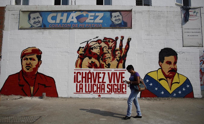 A woman walks past a mural depicting former Venezuelan President Hugo Chavez and incumbent President Nicolas Maduro.