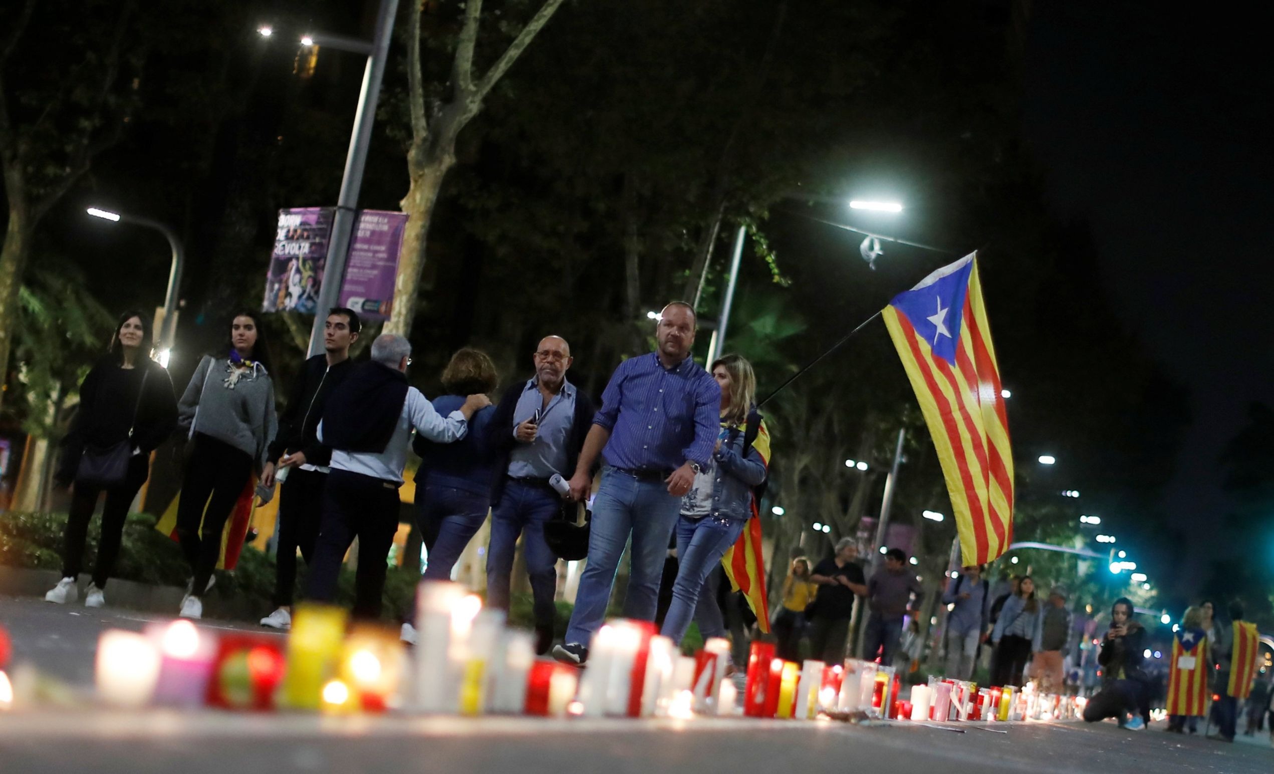 People walk with an Estelada (Catalan separatist flag) next to candles during a protest against the imprisonment of leaders of two of the largest Catalan separatist organizations who were jailed by Spain's High Court, in Barcelona, Spain, Oct. 17, 2017.