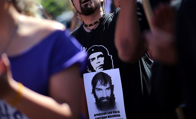 A man wearing a t-shirt with the image of Che Guevara shows a portrait of Santiago Maldonado.