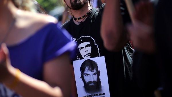 A man wearing a t-shirt with the image of Che Guevara shows a portrait of Santiago Maldonado.