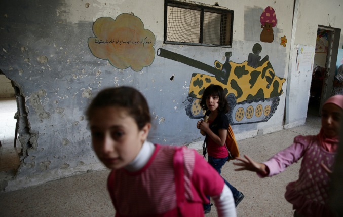 Girls walk through a A damaged corridor inside a school in the town of Douma, eastern Ghouta in Damascus, Syria May 24, 2016, where the war-themed grafitti reads in Arabic, 