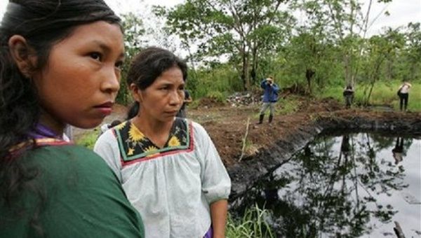 Cofan indigenous Women from Ecuador at the foot of the water body that shows the ecological destruction by the oil company..