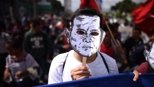A protester wears a mask depicting Guatemala President Jimmy Morales during a large march.