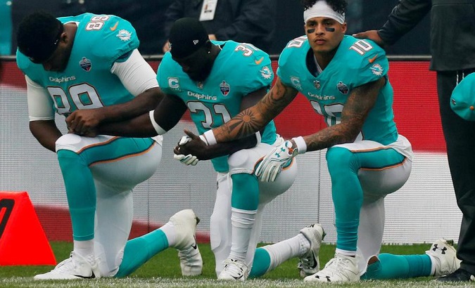 Miami Dolphin players are shown taking a knee during the national anthem.