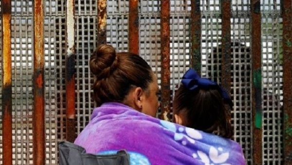 A woman carries her son while talking to her husband across the fence separating Mexico and U.S, as photographed from Tijuana, Mexico.