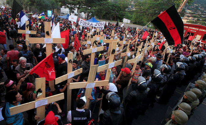 Honduran protesters hold aloft wooden crosses in front of security forces guarding the U.S. Embassy.