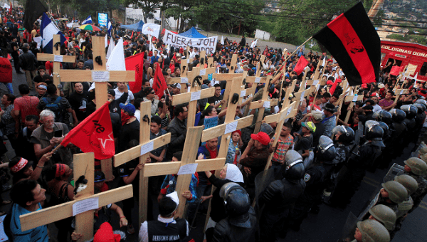 Honduran protesters hold aloft wooden crosses in front of security forces guarding the U.S. Embassy.