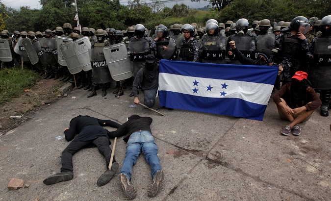 Opposition supporters hold a Honduran flag as others lie on the floor in front of security forces during a protest in Tegucigalpa, Honduras, Dec. 22, 2017.