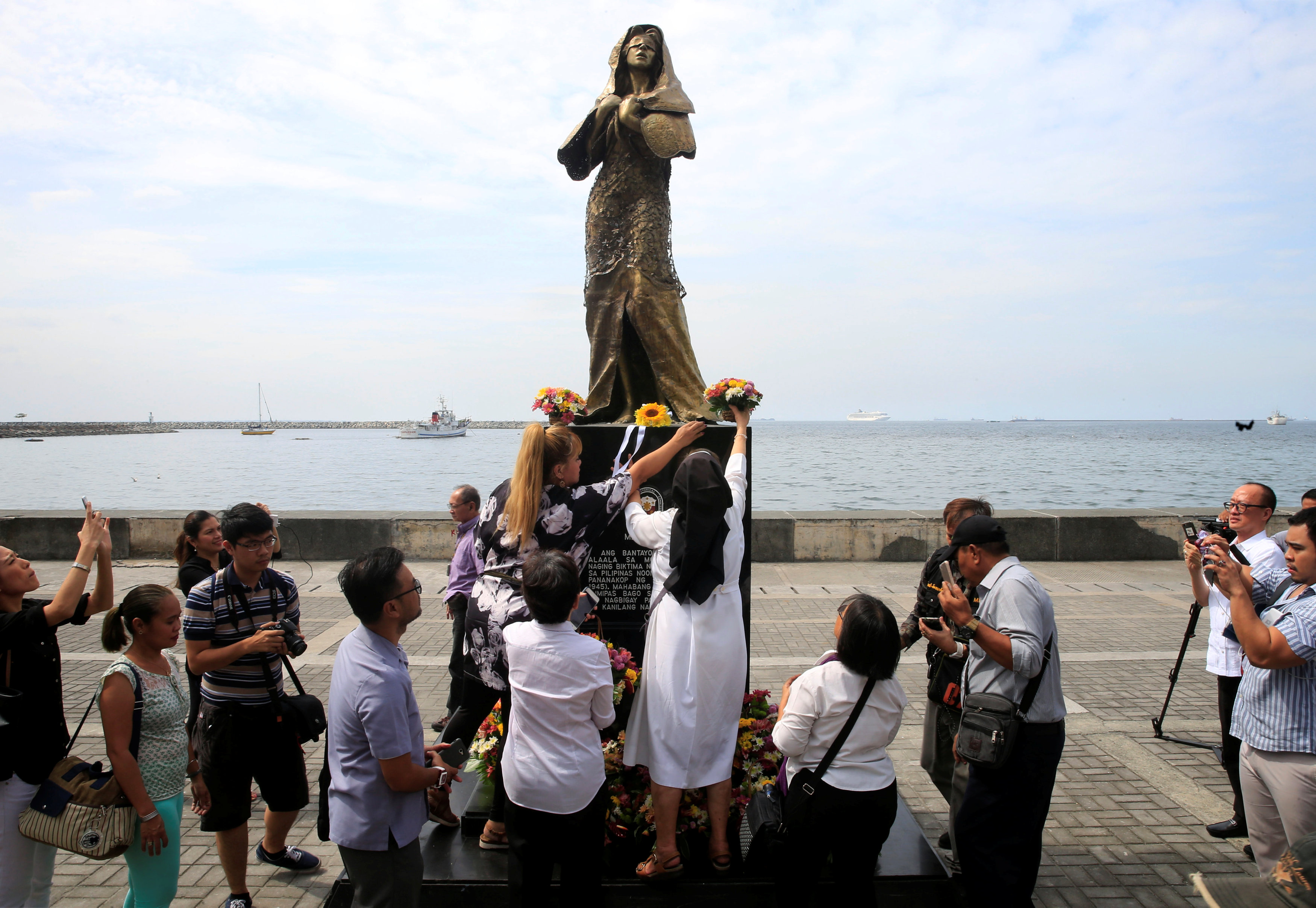 Religious group and non-government organizations offer flowers at a memorial statue that commemorates the Filipino 