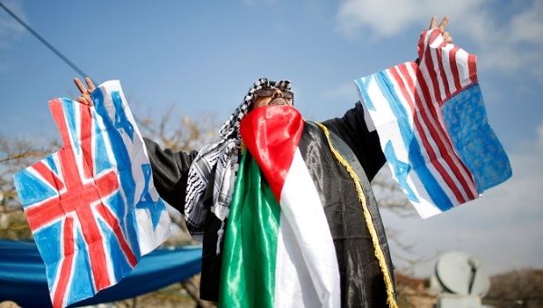 Palestinian demonstrator holds Israeli, British and U.S. flags before burning them during a protest against a U.S. decision to cut aid, in Gaza City