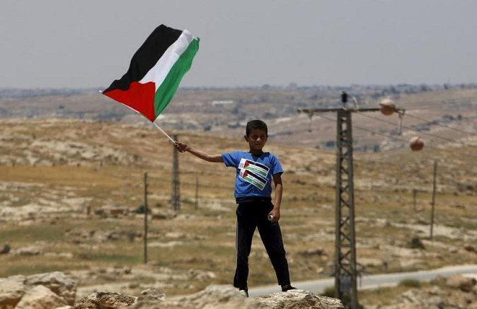 A Palestinian Bedouin boy holds a Palestinian flag during a protest against Jewish settlements in Susya village south of the West Bank city of Hebron June 5, 2015.