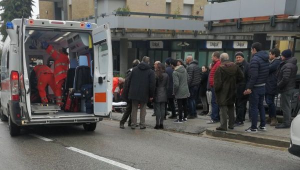 People look at healthcare personnel taking care of an injured person after being shot by gunfire from a vehicle, in Macerata, Italy, February 3, 2018.