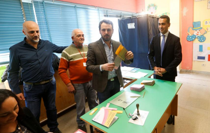 5-Star Movement leader Luigi Di Maio (R) receives his ballot as he prepares to cast his vote at a polling station in Pomigliano d'Arco, near Naples, Italy March 4, 2018.