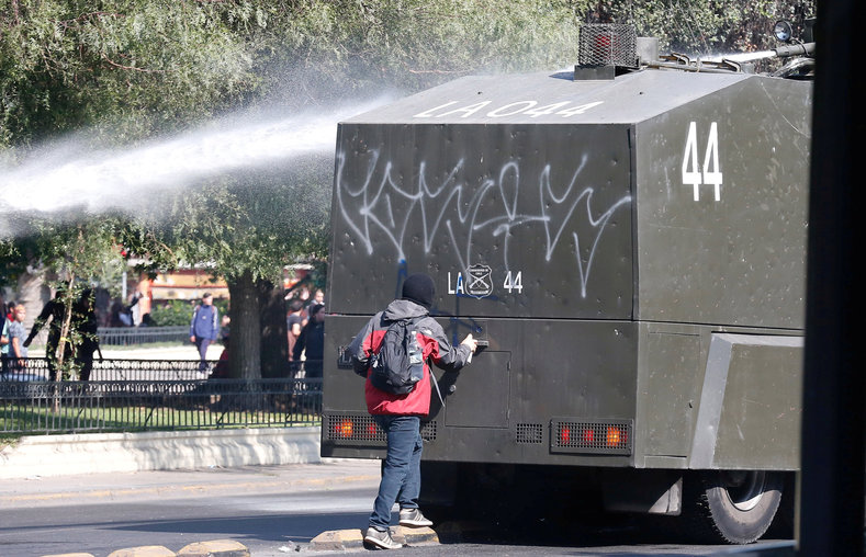 A protester spray paints a riot police vehicle.