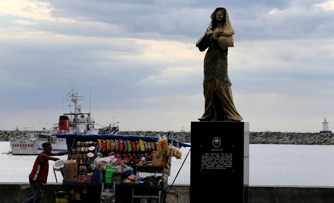 A vendor pushes a cart past a memorial statue that commemorates the Filipino 