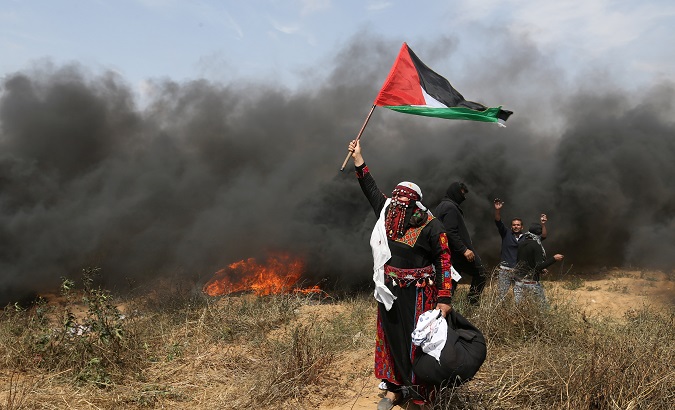 A woman demonstrator holds a Palestinian flag during clashes with Israeli troops at a protest at the Israel-Gaza border, April 27, 2018.