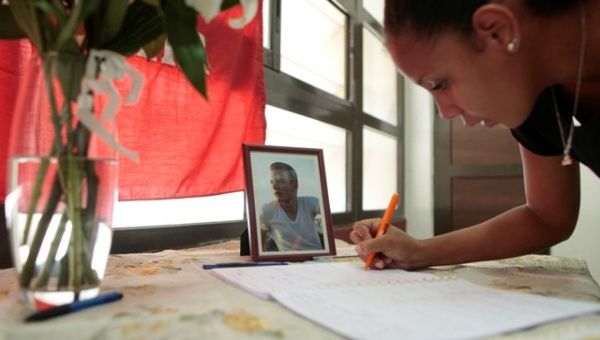 A student writes in a book of condolences dedicated to her classmate Jose Carlos Figueroa, shown in the picture beside the book, at the University of Havana, Cuba.