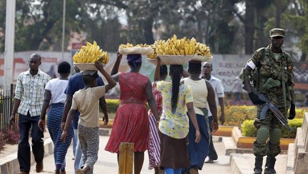 Women carry baskets of banana as they walk past a military personnel patrolling in Kampala, Uganda