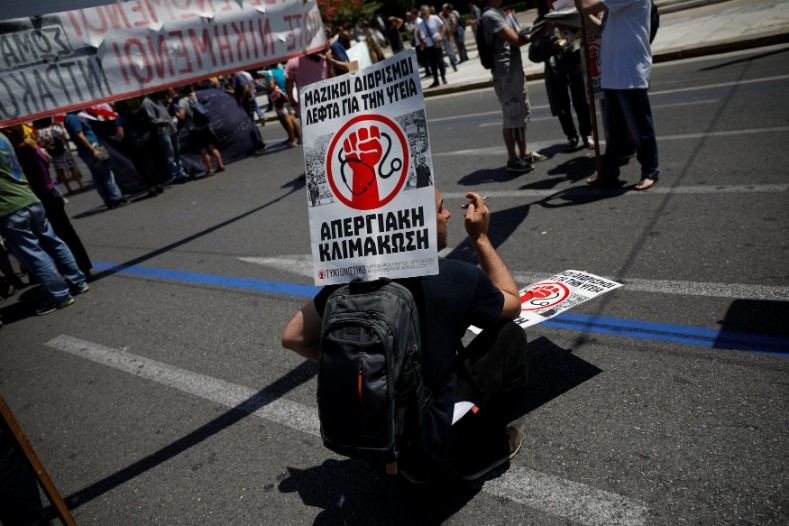 A protester smokes a cigarette during a demonstration marking a 24-hour general strike against planned austerity measures in front of the parliament building. The placard reads 