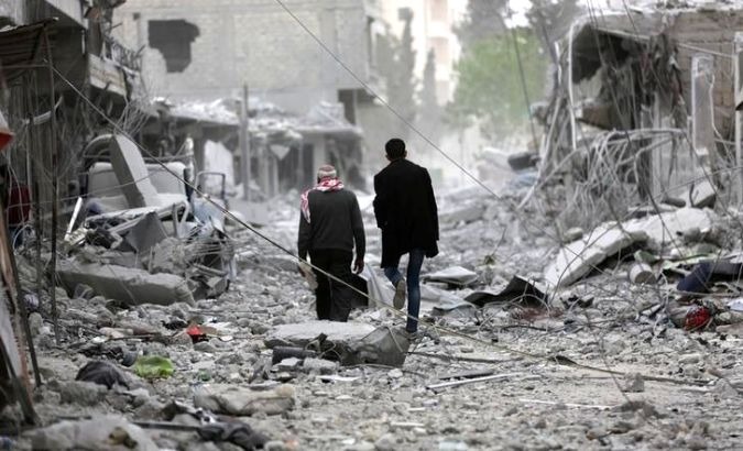 Two people walk through a destroyed region of Syria on March 24, 2018.
