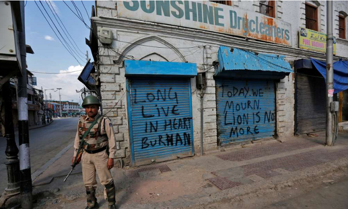 An Indian policeman stands guard in front of the closed shops painted with graffiti during a curfew in Srinagar.