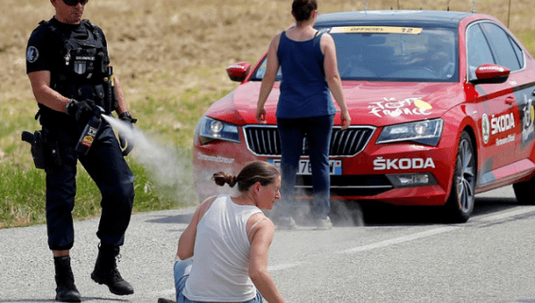 A police officer pepper sprays a protester as another protester stands in front of the race director's car during stage 16. 