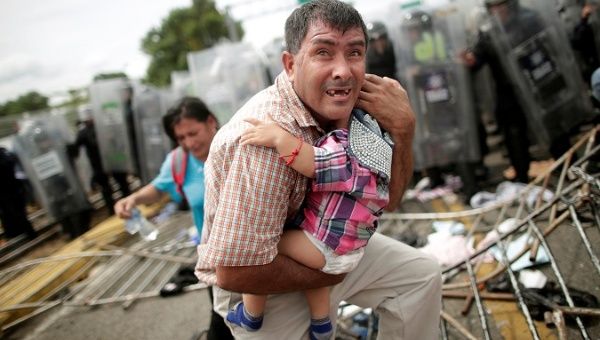 A Honduran man protects his child after fellow migrants stormed a border checkpoint in Guatemala.