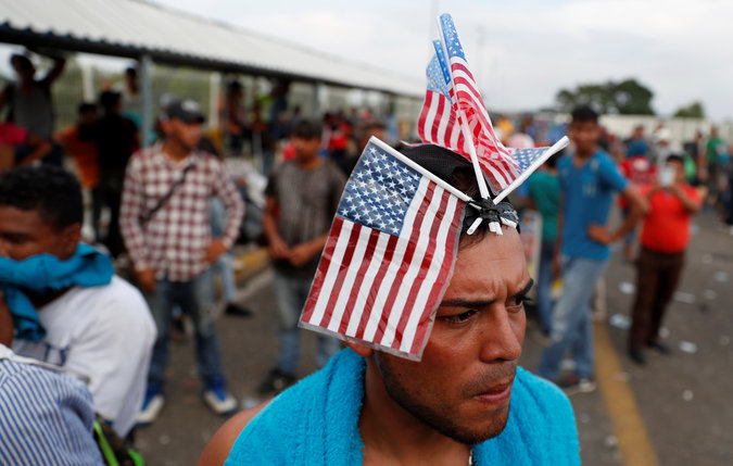 A migrant, part of a caravan of thousands of migrants from Central America en route to the United States, wears a U.S flag on his head waits o cross the border into Mexico and carry on her journey, in Tecun Uman