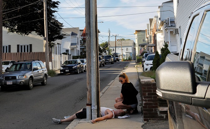 A woman crouches on the sidewalk next to her boyfriend, who is unresponsive and not breathing after an opioid overdose in the Boston suburb of Everett, Massachusetts, U.S., August 23, 2017.