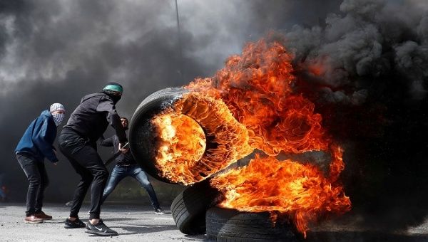 A Palestinian protester moves a burning tire during clashes with Israeli troops near the Jewish settlement of Beit El, in the Israeli-occupied West Bank March 27, 2019. 