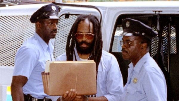 Mumia Abu-Jamal holding a file while being escorted by police.