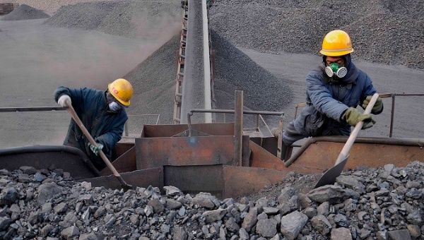 Mine workers shovel a large volume of coal.