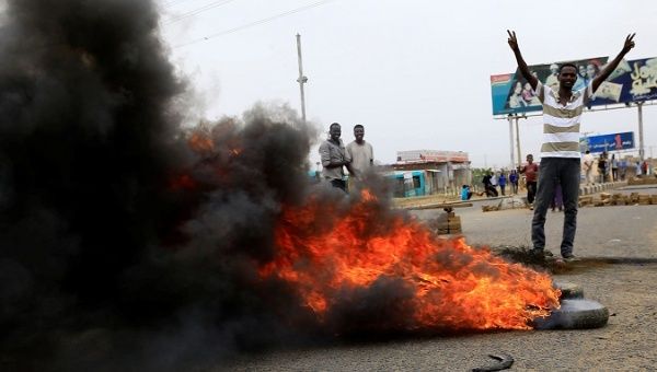 A Sudanese protester gestures near burning tyres used to erect a barricade on a street, demanding that the country's Transitional Military Council handover power to civilians, in Khartoum