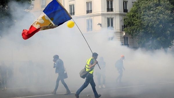 FILE PHOTO: protester in a yellow vest with French flag as tear gas wafts around May Day march with French unions and protesters in Paris, France, May 1, 2019. REUTERS