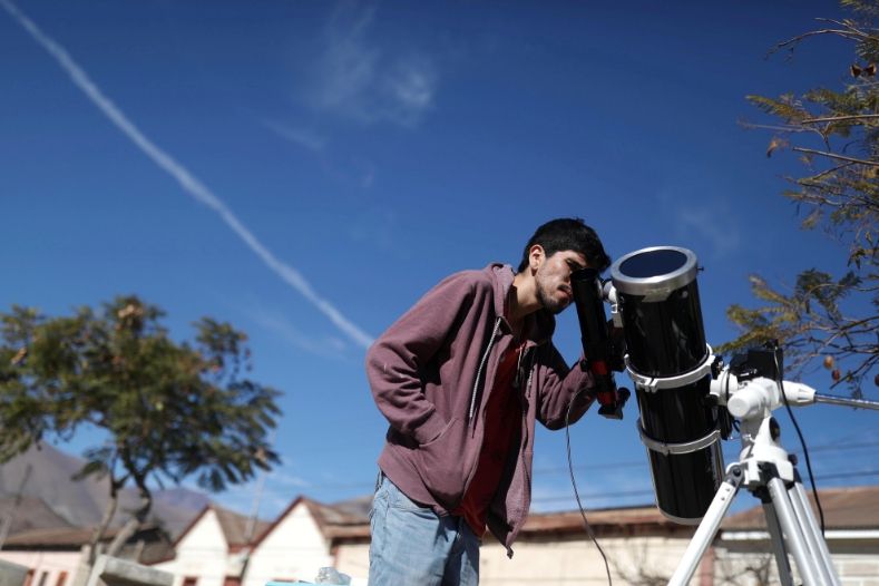 A man observes the sun with his telescope in the street in the town of Vicuna, Chile,