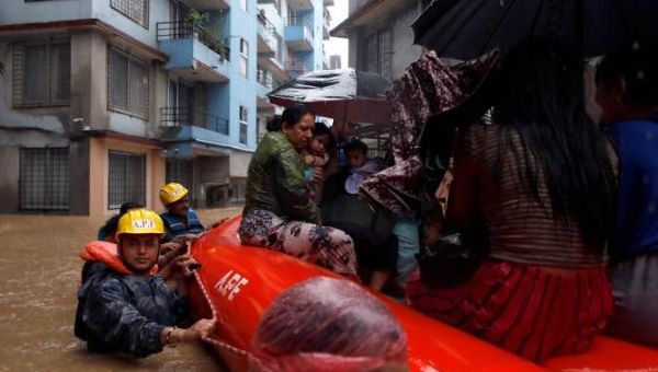 A woman carrying a child is moved by rescue workers towards dry ground from a flooded colony in Kathmandu