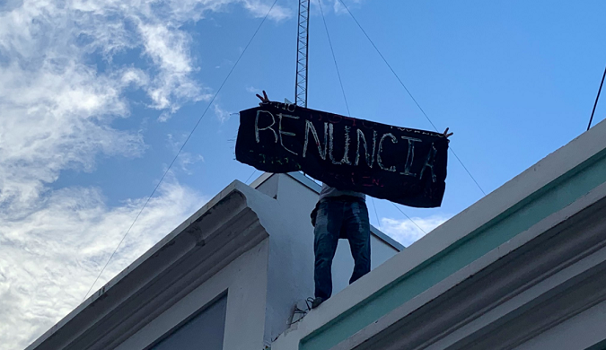 Tito Kayak, a famous Puerto Rican activist climbs onto the roof a police building next to Governor's Rosello Mansion, to unfold a banner asking him to resign.