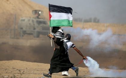 A woman holding a Palestinian flag runs as tear gas fired by Israeli forces during an-anti Israel protest, at the Israel-Gaza border fence in the southern Gaza Strip August 23, 2019. 