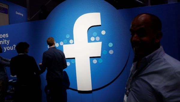 Attendees walk past a Facebook logo during Facebook Inc's F8 developers conference in San Jose, California, U.S., April 30, 2019. 