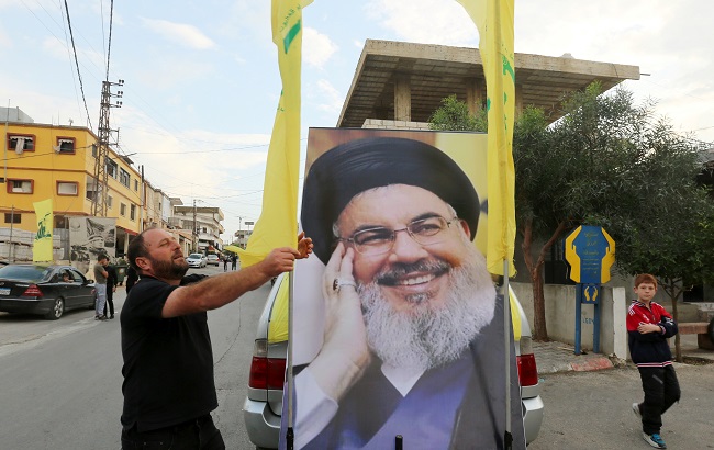 A man adjusts Hezbollah flag on a vehicle decorated with a poster of Lebanon's Hezbollah leader Sayyed Hassan Nasrallah in the southern village of Kfar Kila, Lebanon, October 25, 2019.