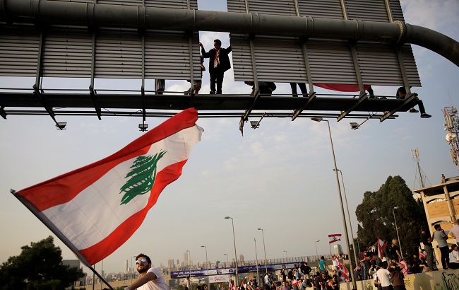 A protester waves a Lebanese flag as another one stands on a road sign at a demonstration blocking the highway during ongoing anti-government protests in Hazmiyeh, Lebanon November 13, 2019.