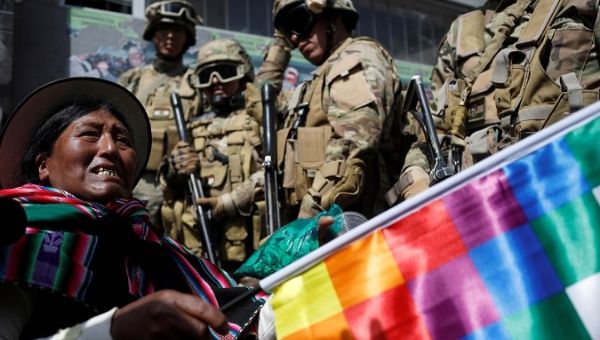 Woman holding a Wiphala flag protests in front of soldiers in La Paz, Bolivia, Nov. 15, 2019.