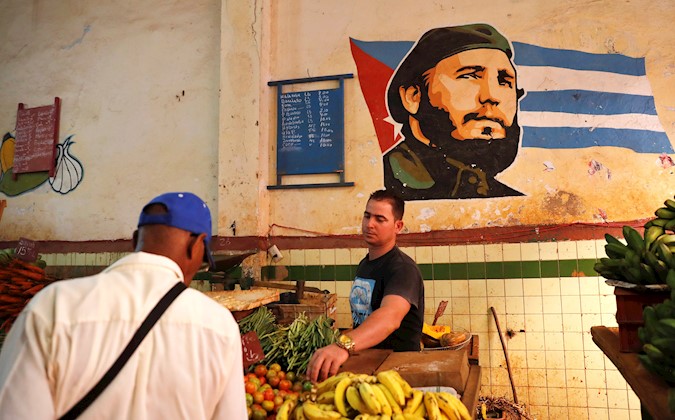 A man buys in an agromercado with the image of Fidel Castro painted on one of its walls