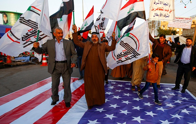 Iraqi people walk on a U.S. flag in a protest after an airstrike at the headquarters of Kataib Hezbollah militia group in Qaim, in the holy city of Najaf, Iraq December 30, 2019.