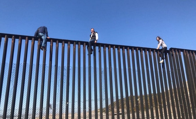 Three migrants climb the U.S. border fence in the city of Tijuana, Mexico, 2019.