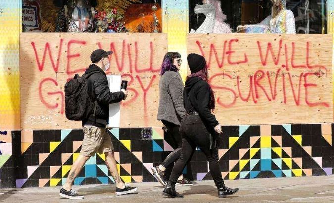 People walk by a boarded up window at a closed store with a message in the Haight-Ashbury district, 'We Will Get By, We Will Survive' in San Francisco, California, USA, 18 March 2020.