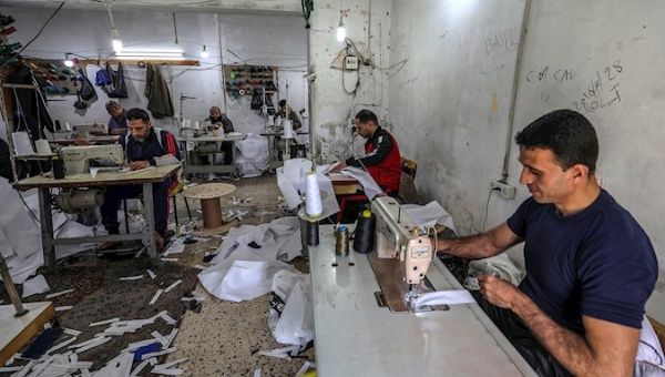 Palestinians manufacture protective coverall suits in a small sewing factory in Gaza City, 30 March 2020