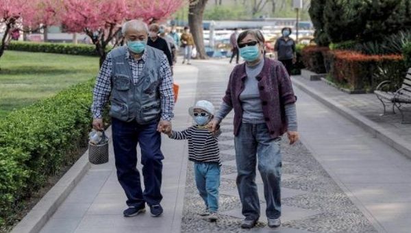 People wearing protective face masks walk in a park in Beijing, China, April 14, 2020. 