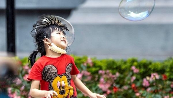 A girl wearing a mask plays with soap balloons in Guangzhou, China, May 1, 2020.